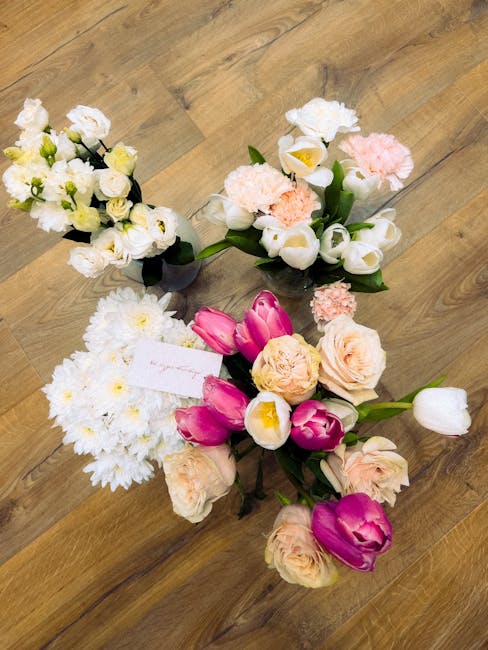A collection of fresh floral arrangements placed on a wooden floor, featuring a variety of flowers in soft pastel and vibrant colours. There are white and cream roses, pink tulips, and white daisies w