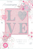 This anniversary card radiates a gentle, enduring romance, echoing the softness of pastel bouquets often delivered around Shepperton's quiet streets. At its centre, the word LOVE appears in softly raised glitter lettering, with pale blush tones and a pearly white finish edged delicately in silver. The letters look slightly cushioned and tactile, inviting touch the way a satin ribbon does when tied around a bouquet. The letterforms rest against a dusky pink background that feels warm yet understated, like the inside of a gift box lined with tissue. Surrounding the central word, an array of delicate blooms unfurls in a loose, almost watercolor style. Blush and mauve petals, slender grey-green leaves, and curling tendrils of foliage weave together, forming a light garland across the card rather than a dense frame. Subtle butterflies and tiny swirls appear here and there, adding a touch of movement and playful elegance, similar to the charm of a cottage garden tucked away off a Shepperton lane. The floral lines are fine and precise, suggesting the practiced hand of a florist used to arranging anniversary flowers for local couples, from homes near the High Street to those closer to the river. Gentle metallic accents-particularly small touches of silver-catch the light at certain points, giving the card a refined shimmer. Scripted phrases such as On Our Anniversary and a promise of continued love are written in a flowing, romantic font. All together, the textures, colours, and motifs create a keepsake that feels as thoughtful and heartfelt as a hand-delivered anniversary bouquet shared in Shepperton.